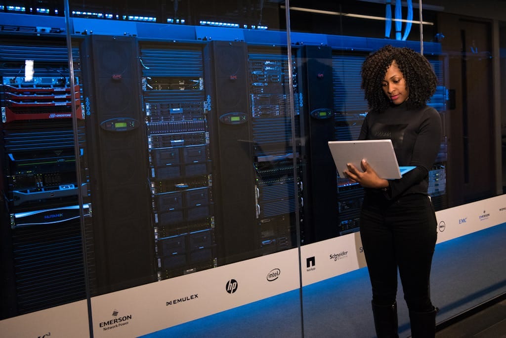 A female engineer using a laptop performing website maintenance in a server room.