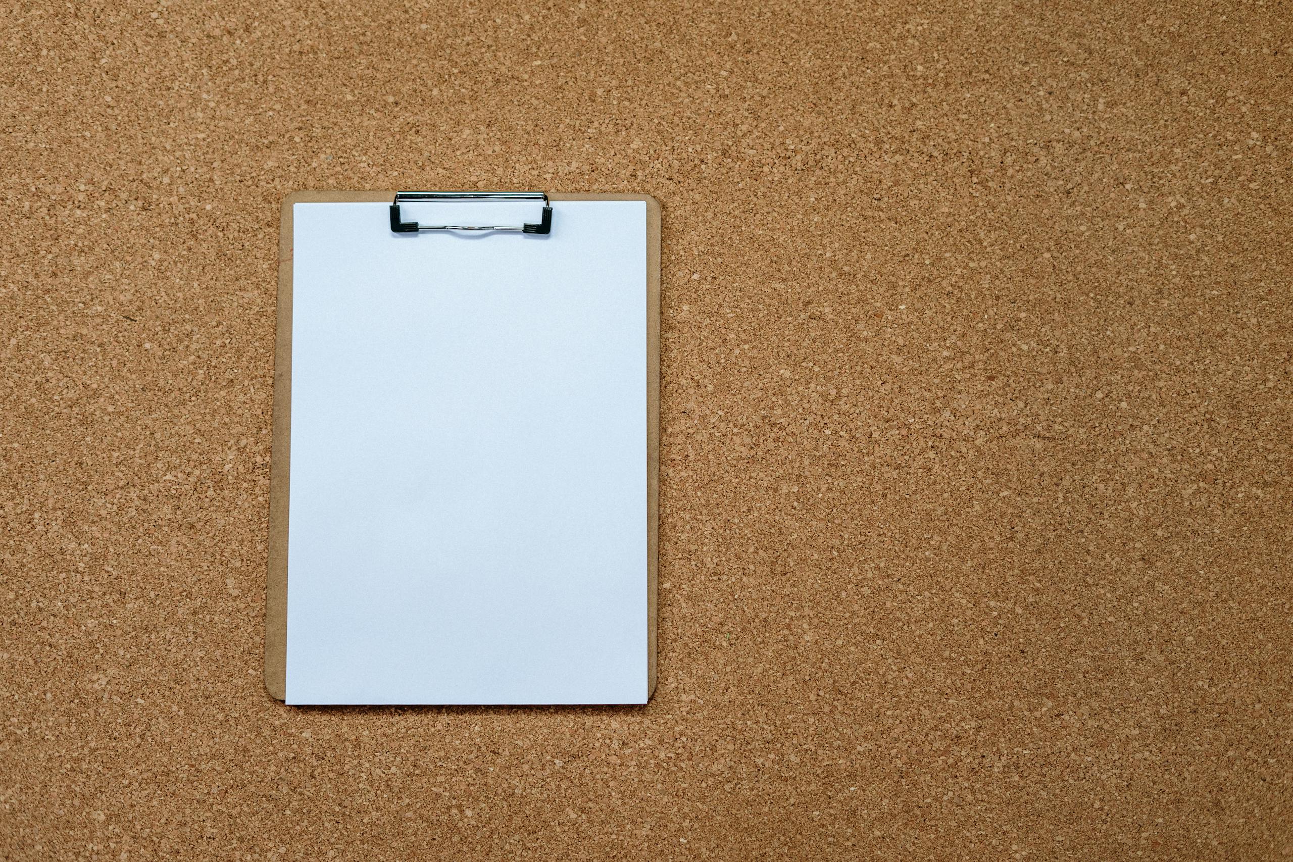 Overhead shot of a blank clipboard on a corkboard, offering ample copyspace.